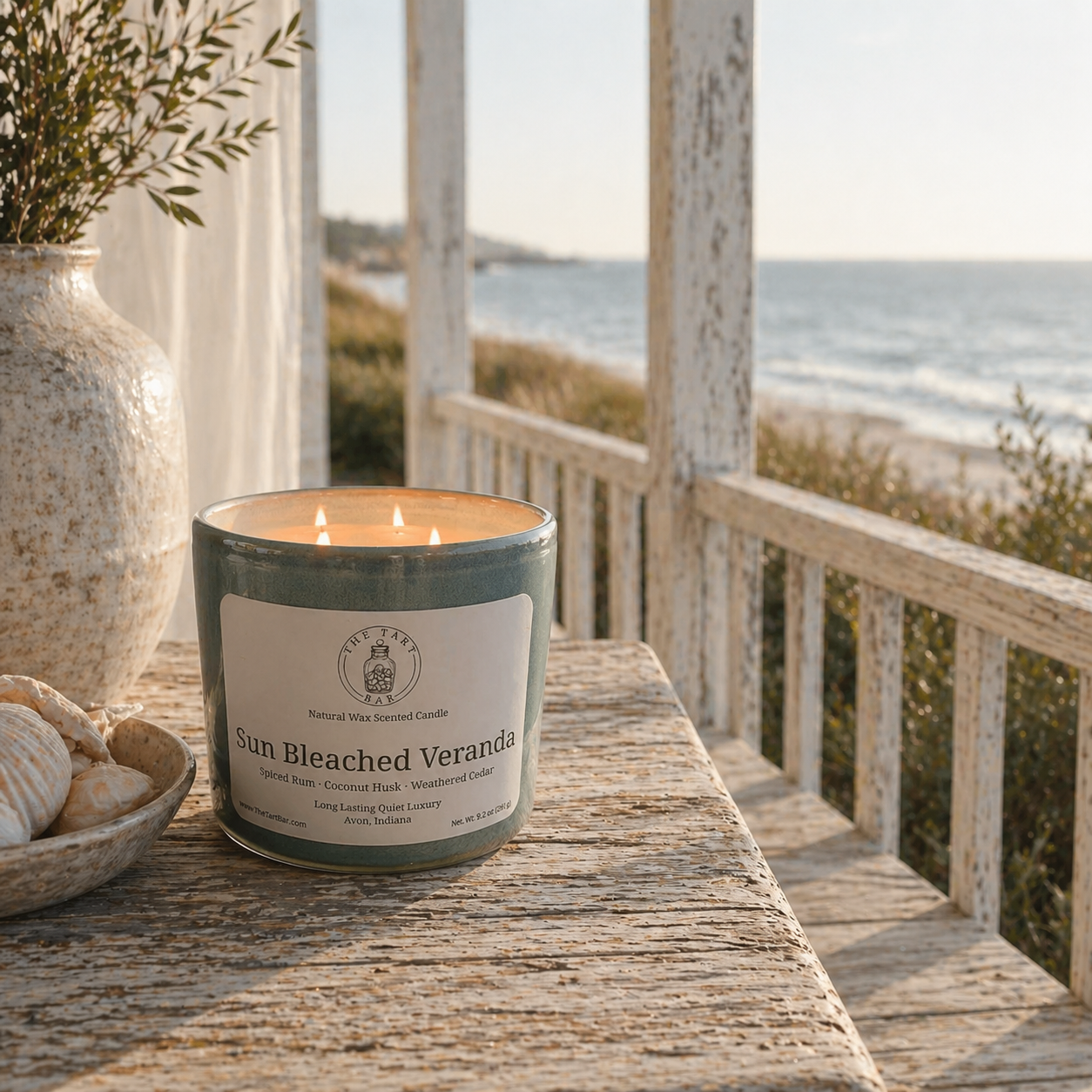 Candle labeled 'Sun Bleached Veranda' on a wooden surface with a beach view in the background