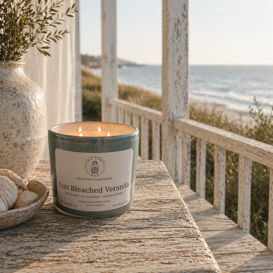 Candle labeled 'Sun Bleached Veranda' on a wooden surface with a beach view in the background